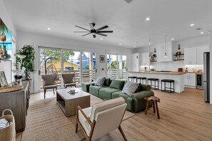 A spacious living area with a green sofa, a coffee table, and a dining area with a kitchen in the background. - Brand New, Heated Pool/Spa, Minutes to Beach (Bradenton Beach)