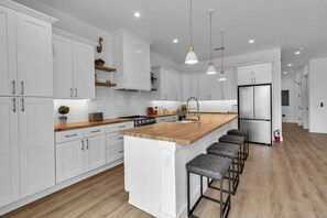 A modern kitchen with white cabinets, a wooden countertop, a central island with bar stools, and a stainless steel refrigerator. - Brand New, Heated Pool/Spa, Minutes to Beach (Bradenton Beach)