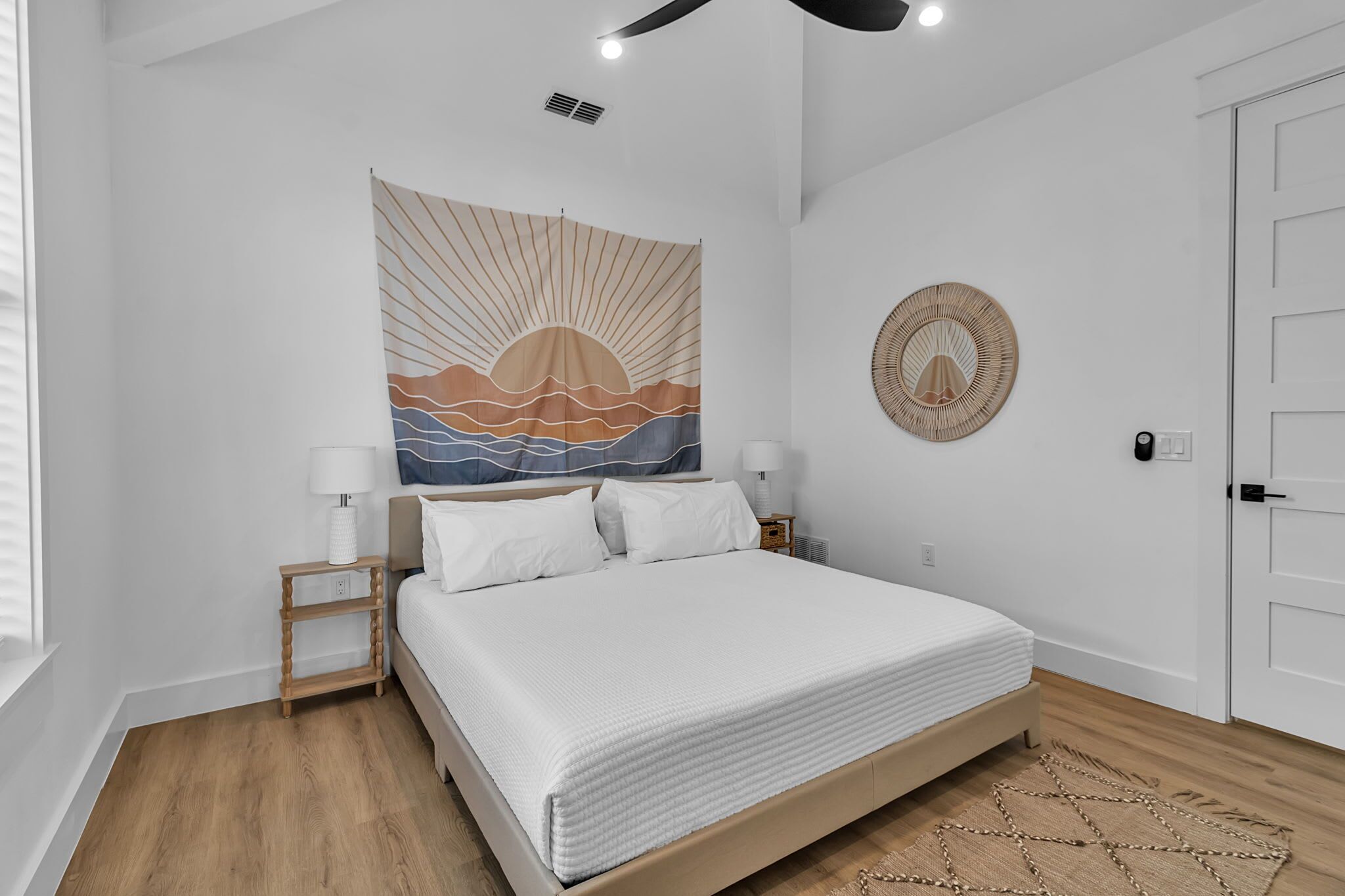 A bedroom with a bed, bedside tables, a tapestry, a woven wall hanging, and a door.
