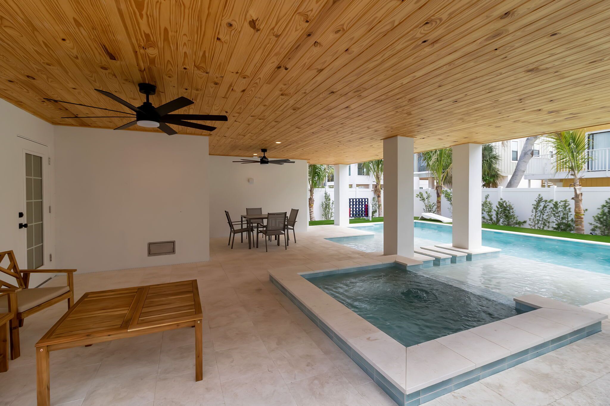 Ein überdachter Außenbereich mit Pool, Holzmöbeln und Deckenventilatoren.
