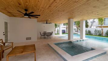 Ein überdachter Außenbereich mit Pool, Holzmöbeln und Deckenventilatoren.