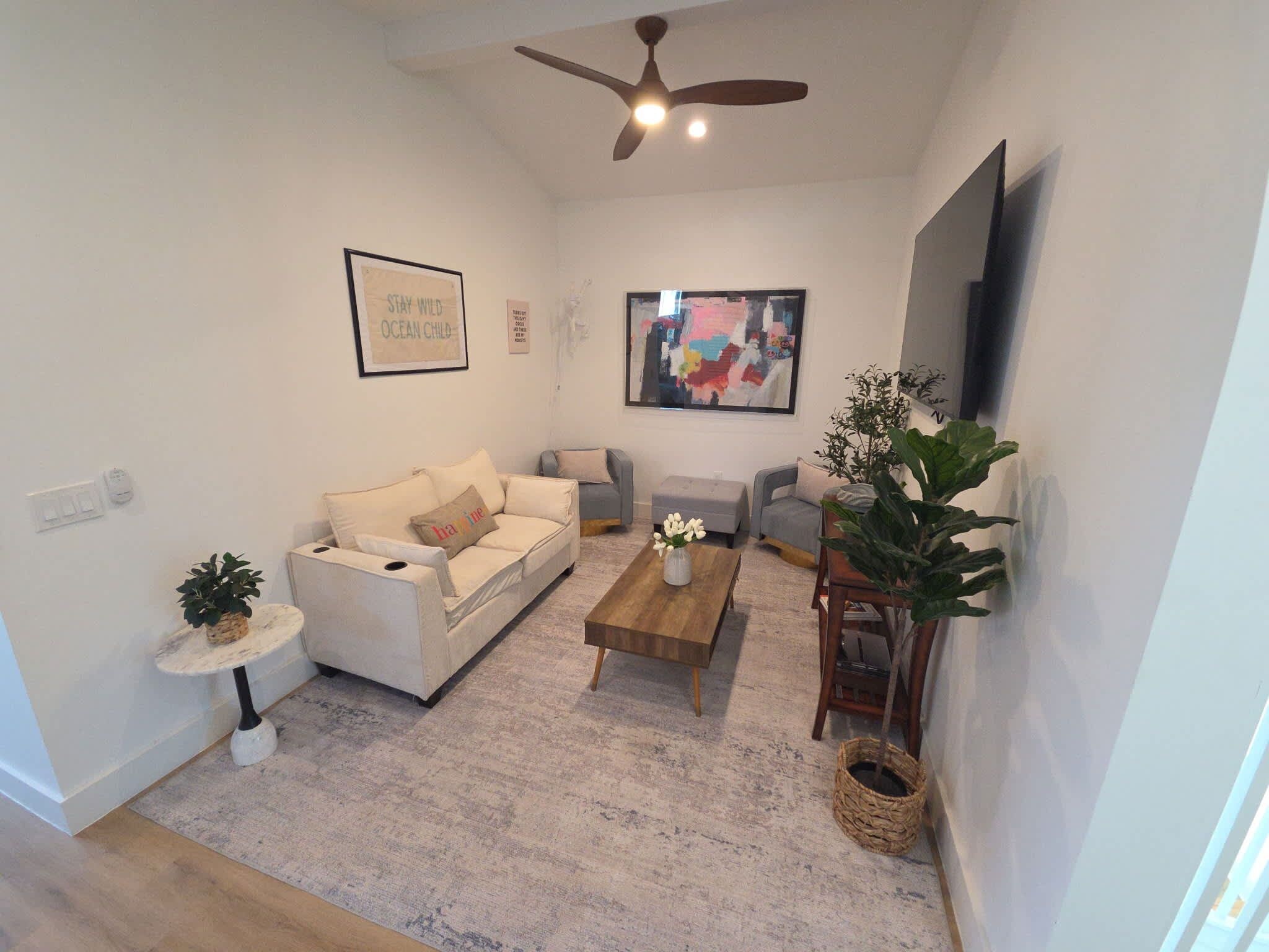 A living room with a sofa, a coffee table, a TV, and a ceiling fan.