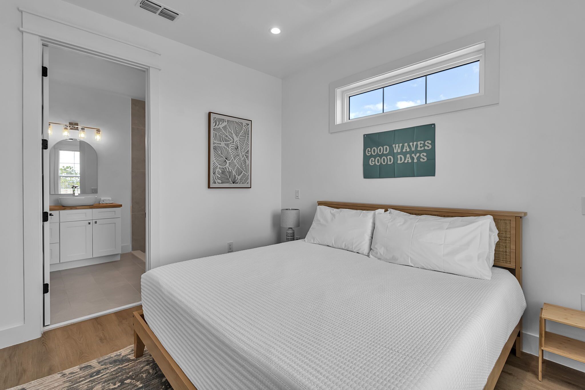 A bedroom with a bed, a window, a door, a mirror, and a wall sign.