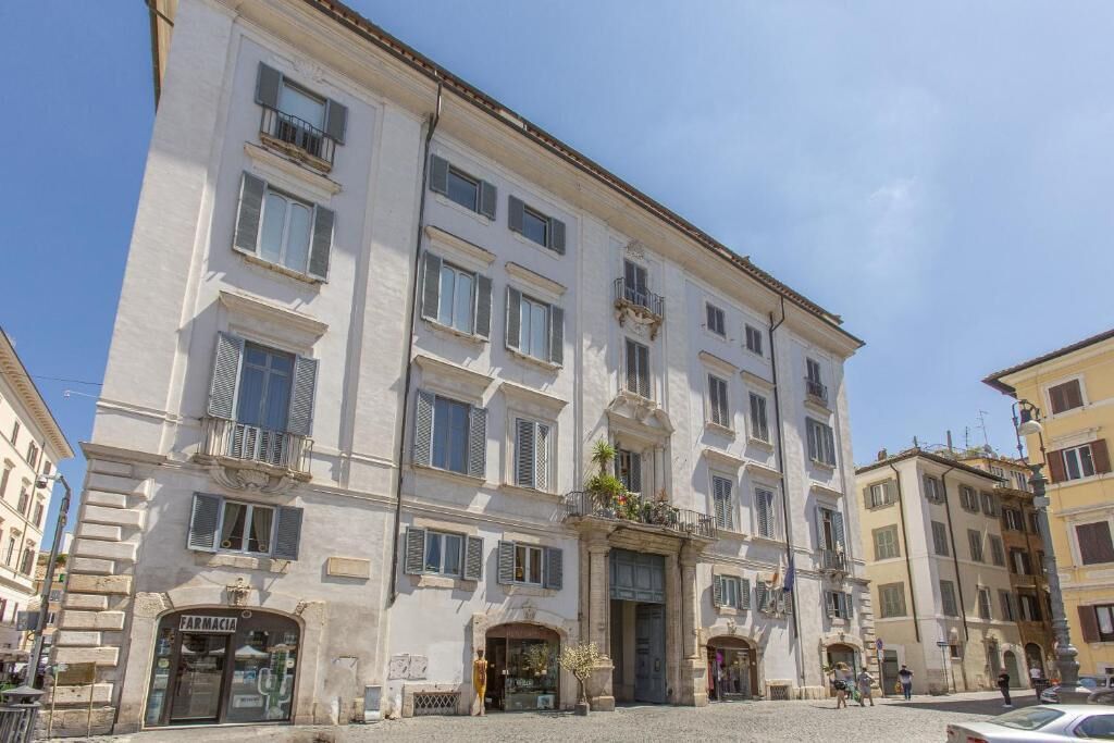 A multi-story building with a ground-floor pharmacy, balconies, and a cobblestone street.