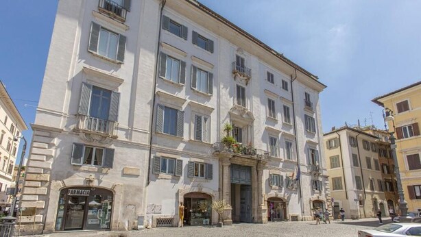 A multi-story building with a ground-floor pharmacy, balconies, and a cobblestone street. - FarneseHouse (Roma)