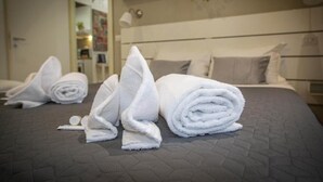A neatly made bed with rolled white towels and a pillow, a bedside lamp, and a wall-mounted shelf with various items. - FarneseHouse (Roma)