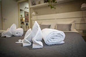 A neatly made bed with rolled white towels and a pillow, a bedside lamp, and a wall-mounted shelf with various items. - FarneseHouse (Roma)
