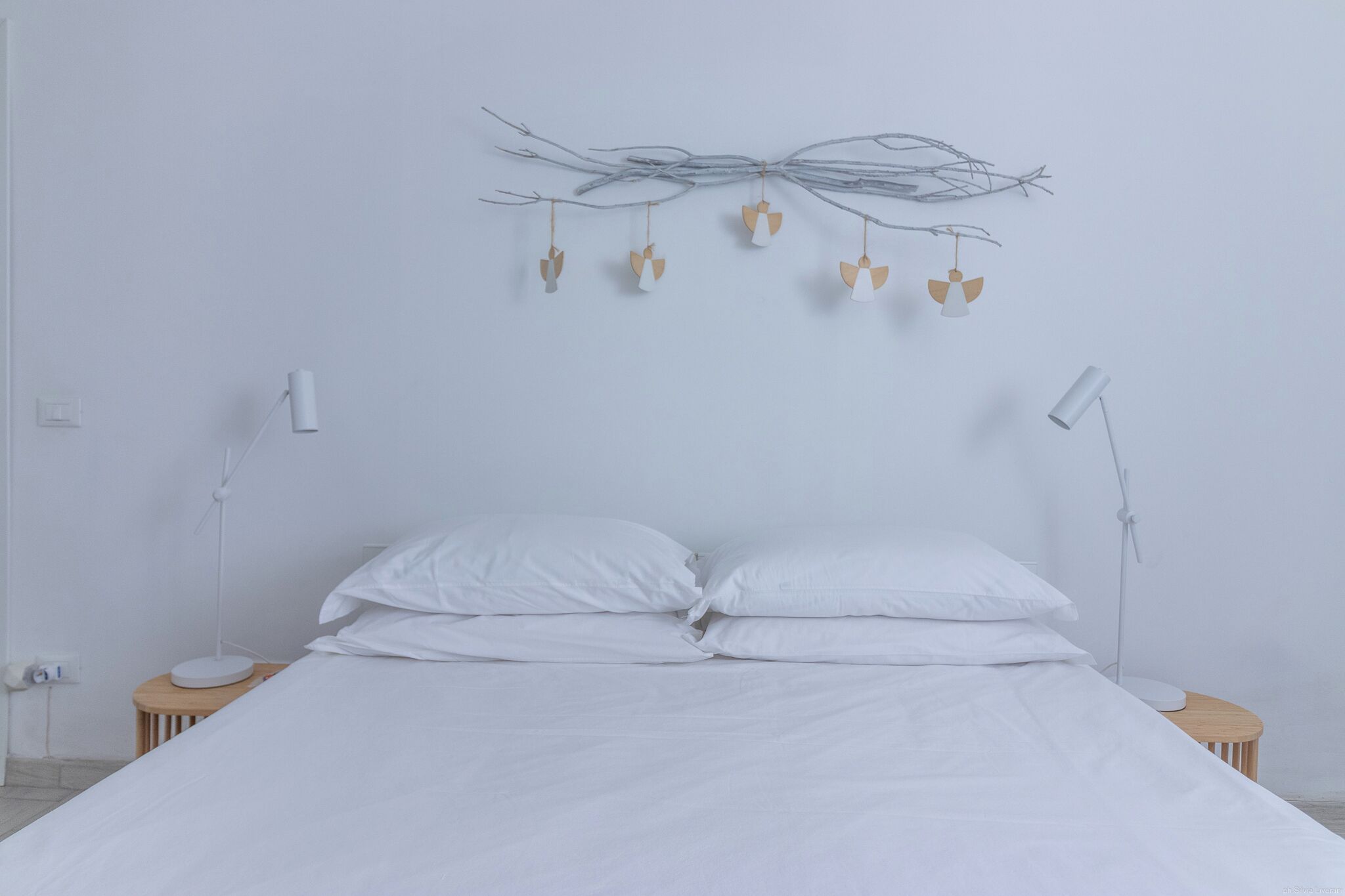 A minimalist bedroom with a large bed, two bedside tables, and a wall-mounted light fixture.