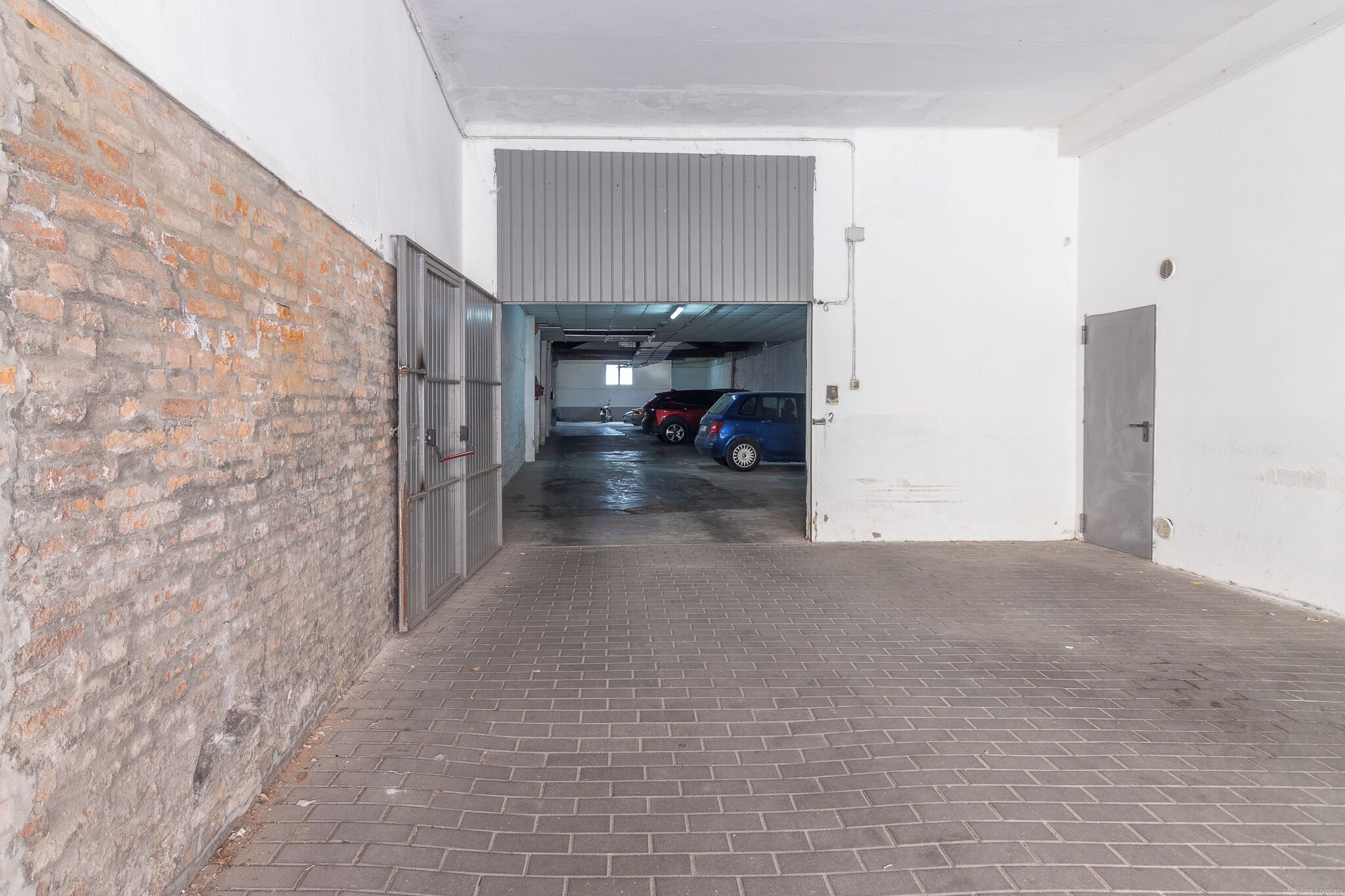 Ein überdachter Parkbereich mit Backsteinwand, Metalltor und Betonboden.