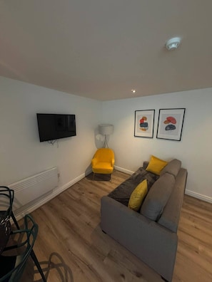 Ein Wohnzimmer mit grauem Sofa, gelbem Sessel und einem flachbildfernseher an der Wand.
