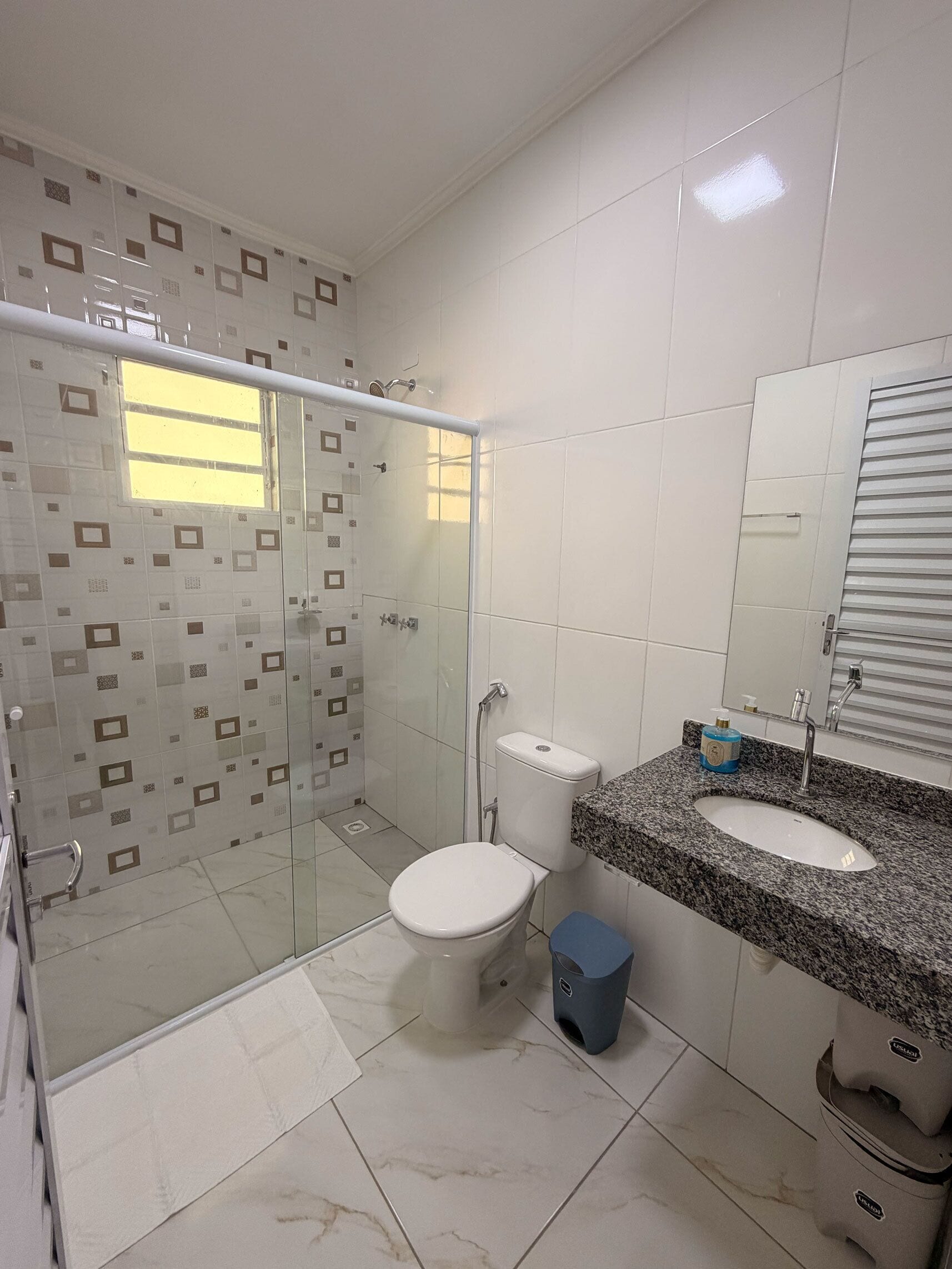 A bathroom with a glass-enclosed shower, a toilet, a sink with a granite countertop, and a mirror.