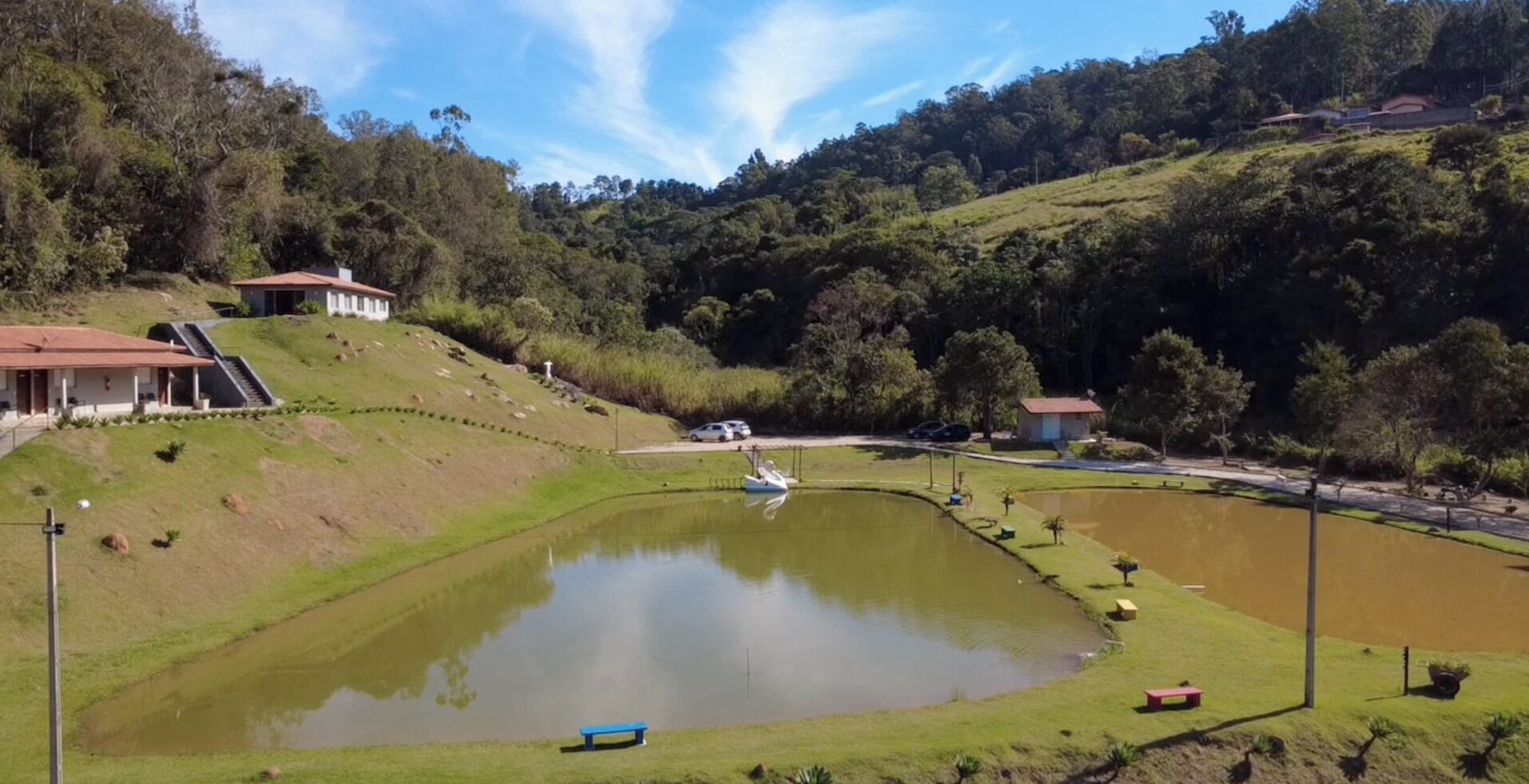 A serene landscape with a pond, a small boat, and a building with a red roof.