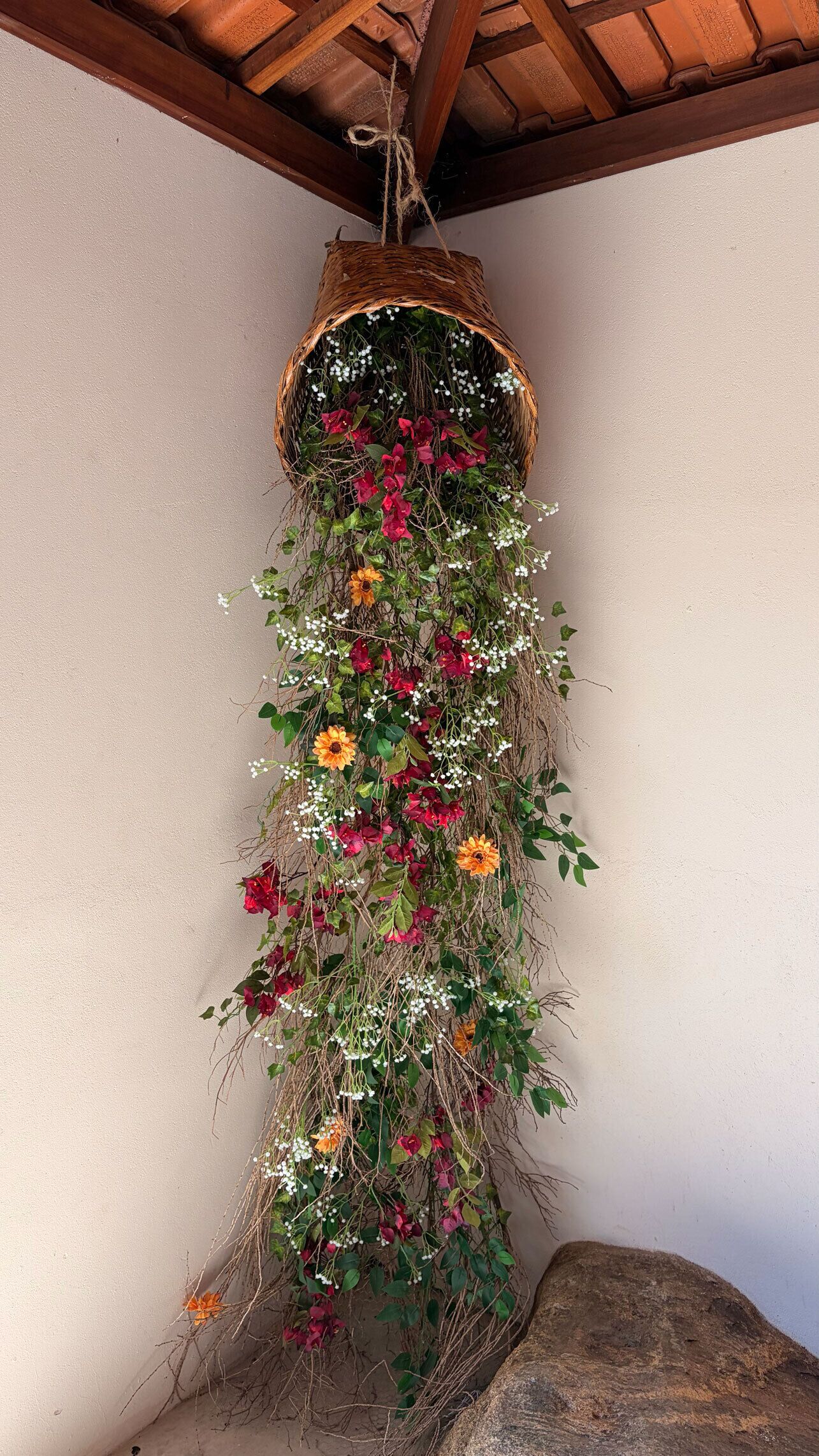 A hanging basket with a variety of flowers and greenery against a wall.