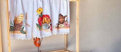 Una estantería de madera con un mantel blanco con ilustraciones de comida, una jarra azul, una jofaina blanca y una olla de cobre.
