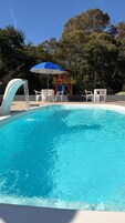 Una piscina con fuente, rodeada de sillas blancas y un parque infantil.