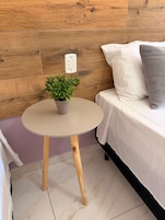 Una mesita redonda con una planta en maceta, un enchufe y una cama con almohadas.