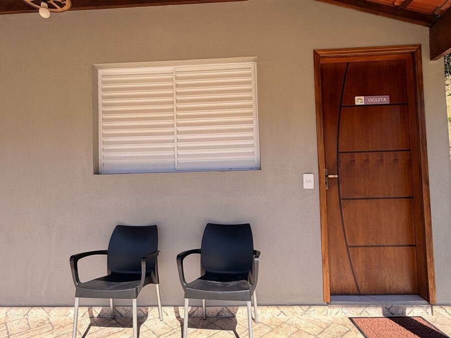 Ein überdachter Außenbereich mit zwei Stühlen, einem mit Jalousien versehenen Fenster und einer Holztür mit Namensschild.