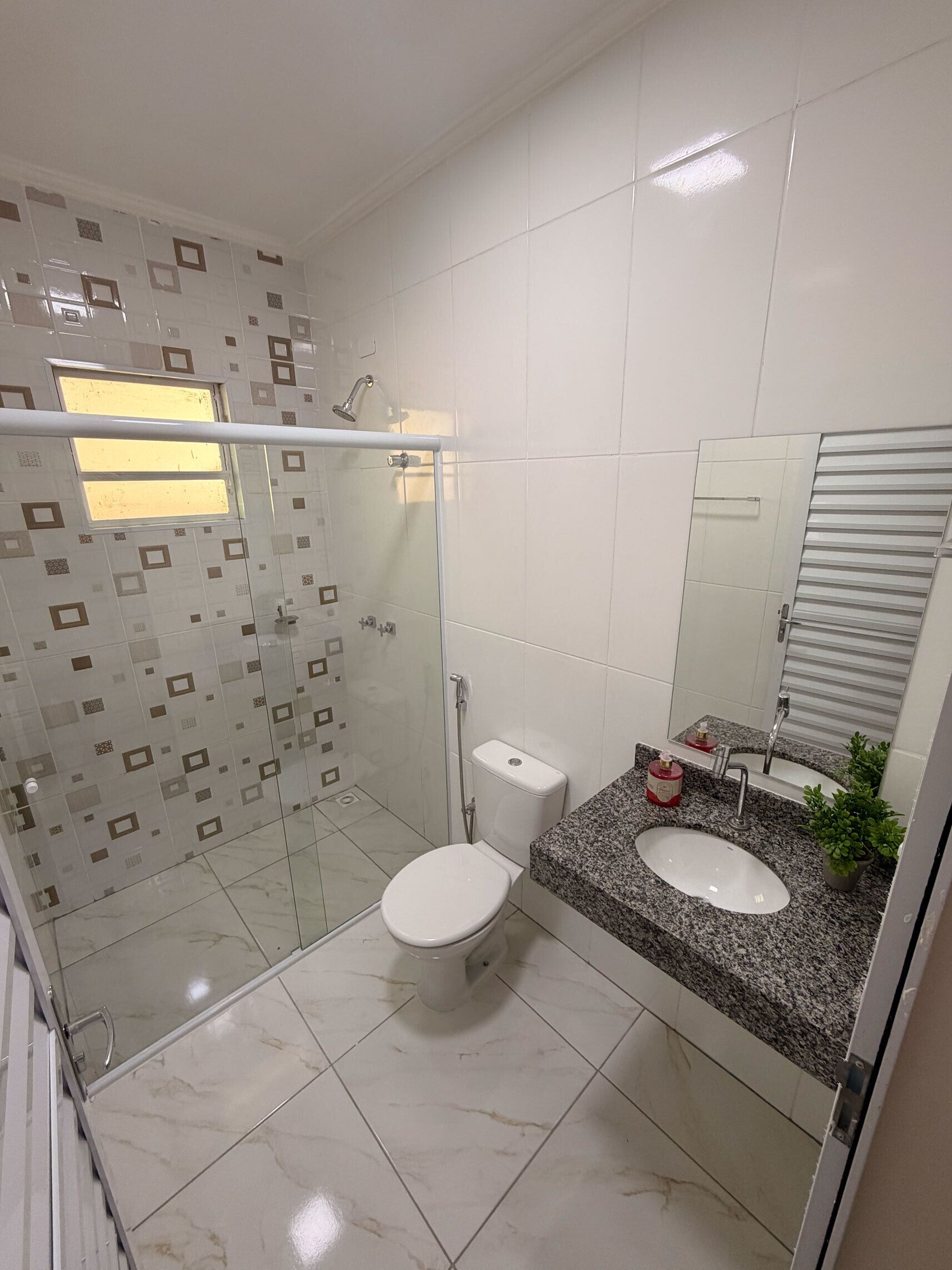 Un baño moderno con ducha de vidrio, inodoro e lavamanos de granito con espejo.