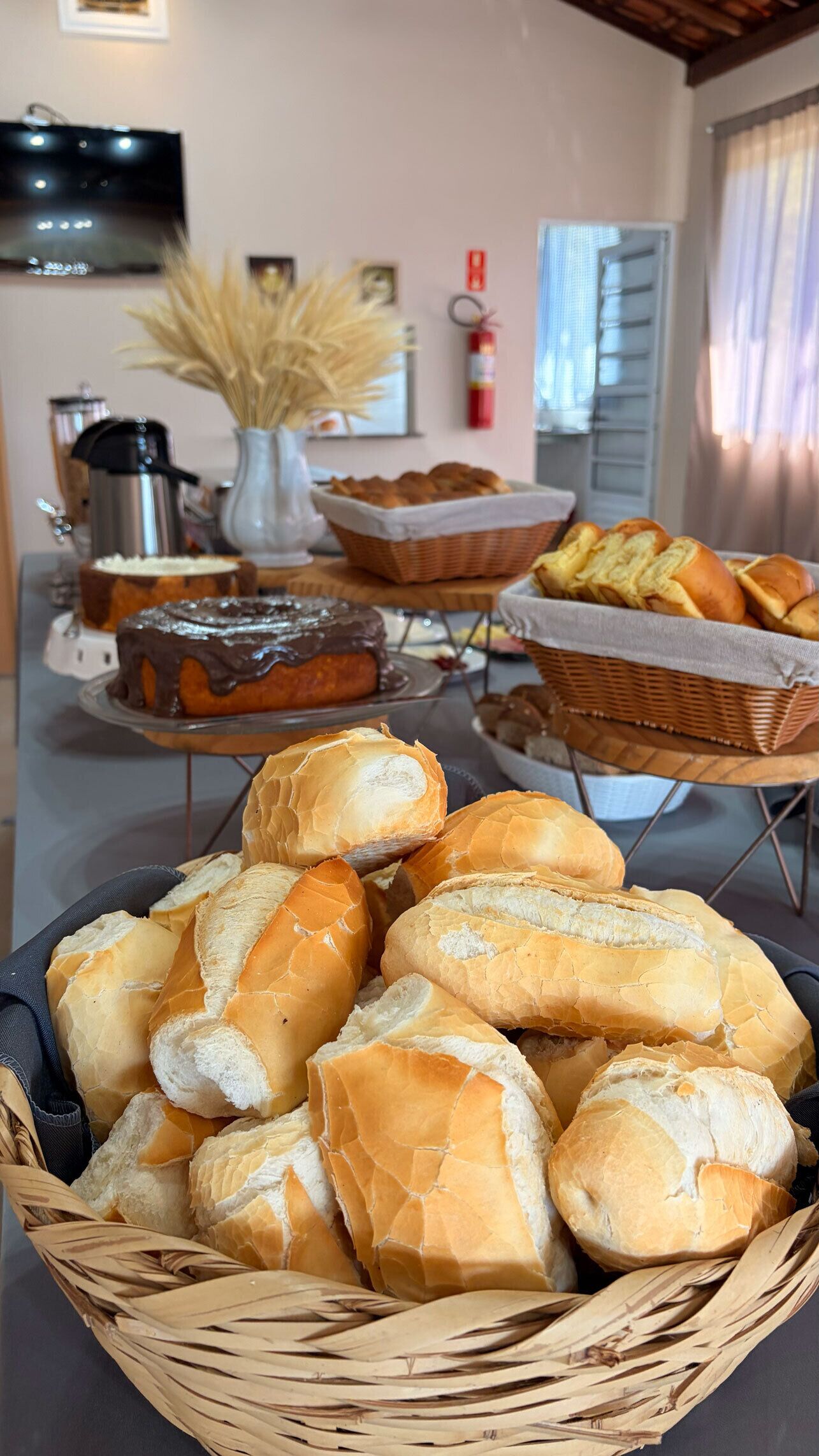 A room with a dining table set with bread, a cake, and a vase with dried plants.