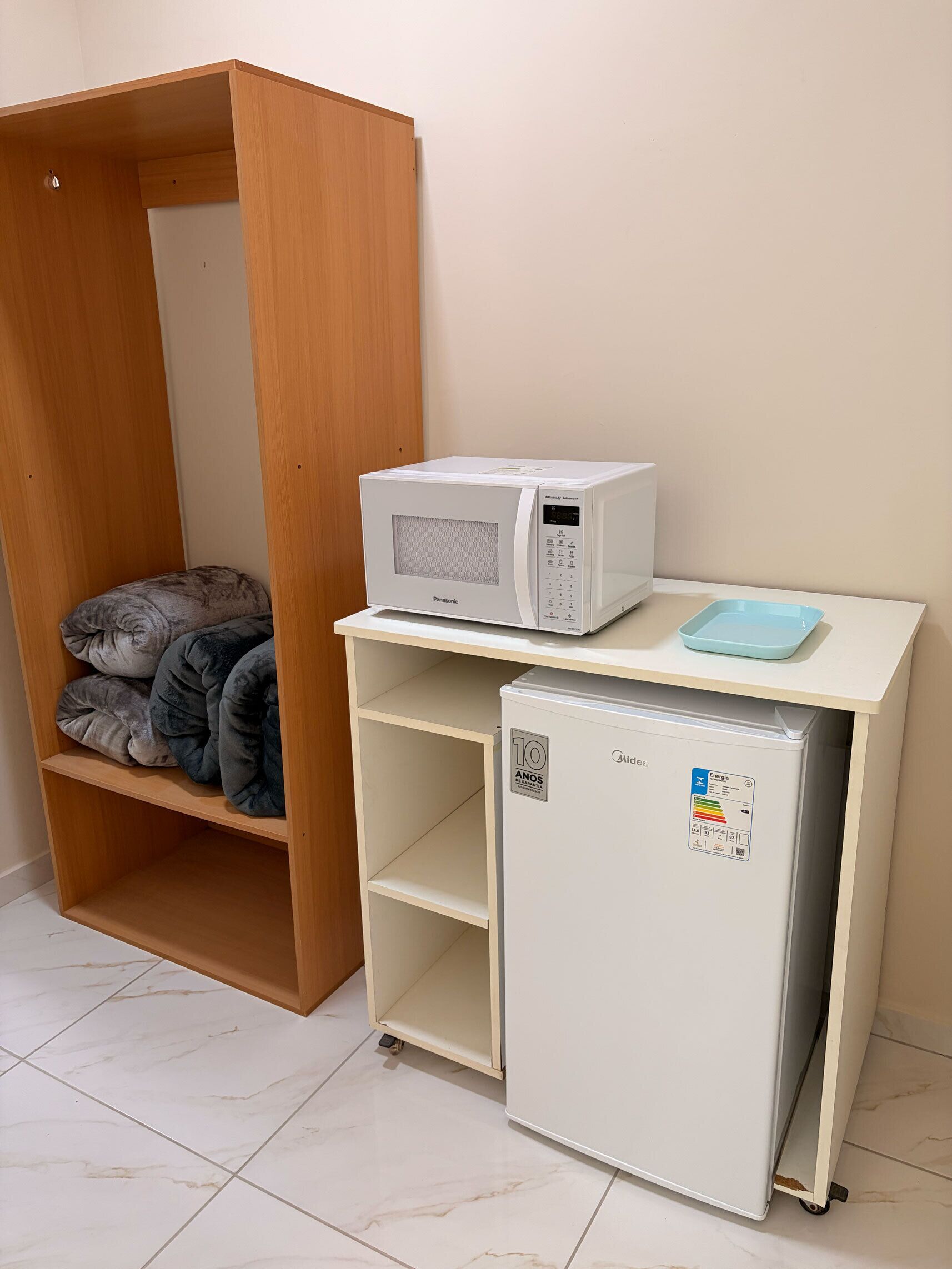 Eine kleine Küchenzeile mit einer Mikrowelle, einem kleinen Kühlschrank und einem Regal mit zusammengefalteten Decken.