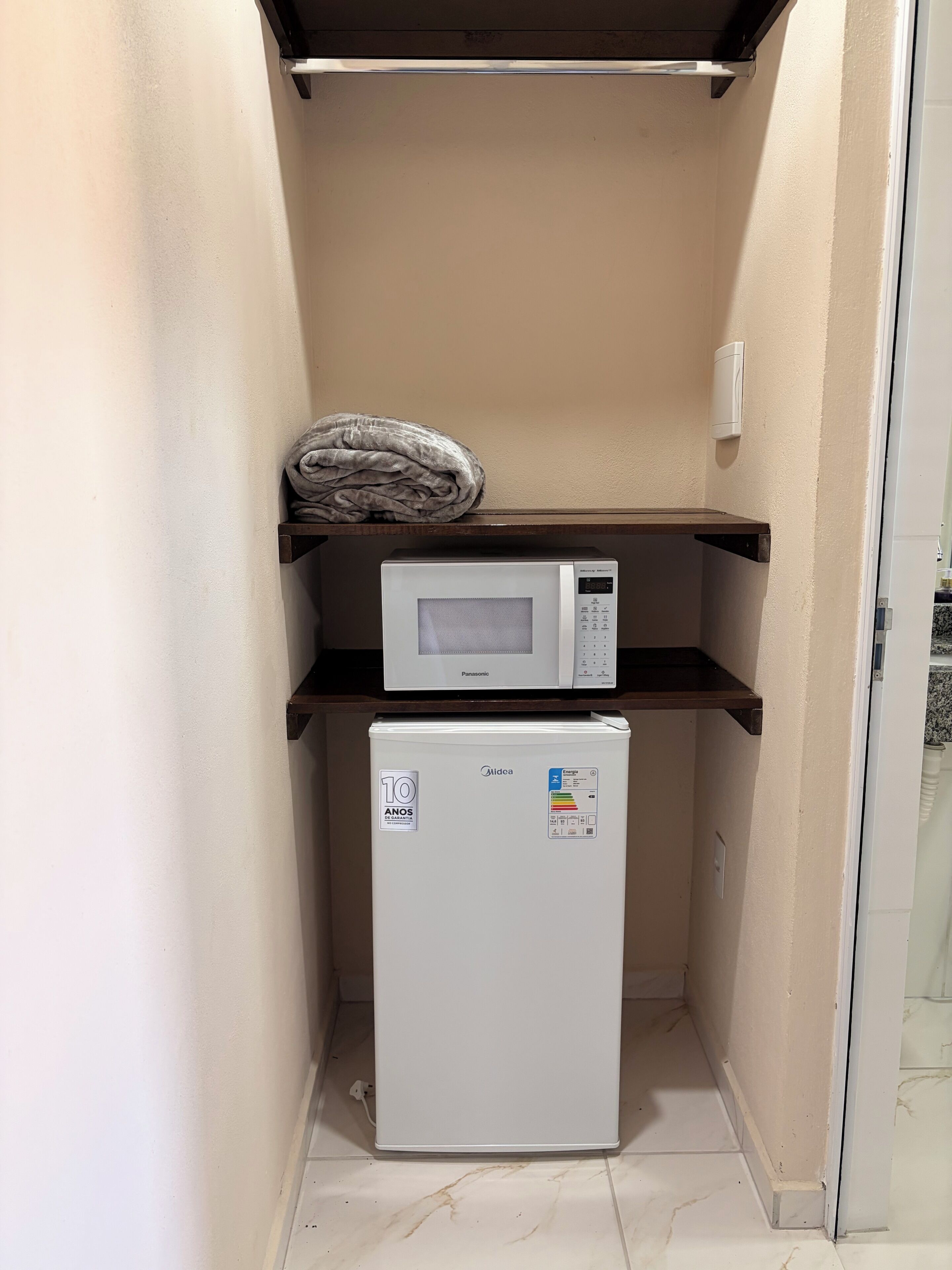 Una kitchenette compacta con microondas y refrigerador, una toalla en el estante superior y una pequeña encimera.