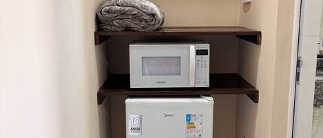 Una kitchenette compacta con microondas y refrigerador, una toalla en el estante superior y una pequeña encimera.