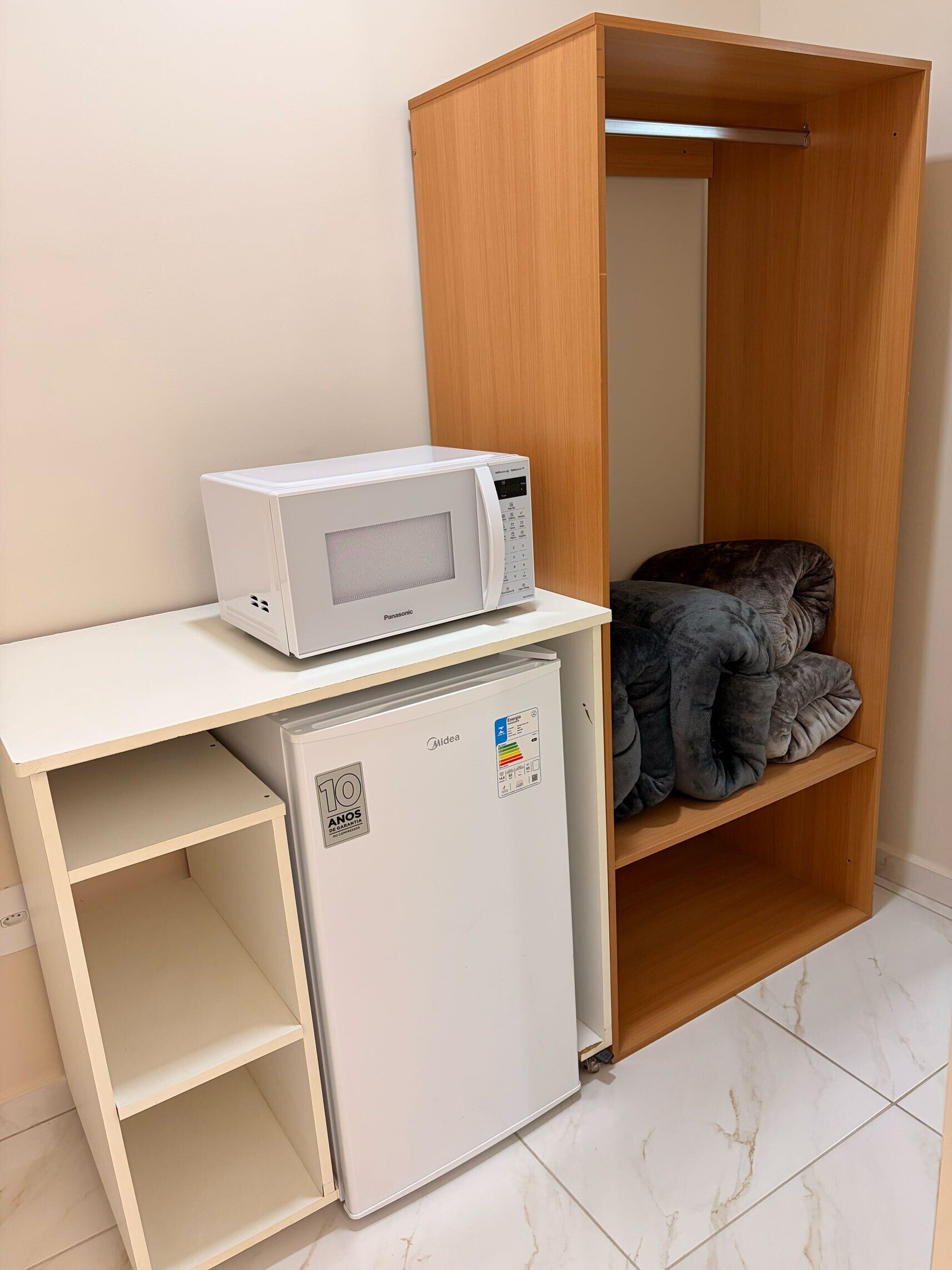Una kitchenette compacta con microondas, refrigerador y un pequeño estante con una manta.