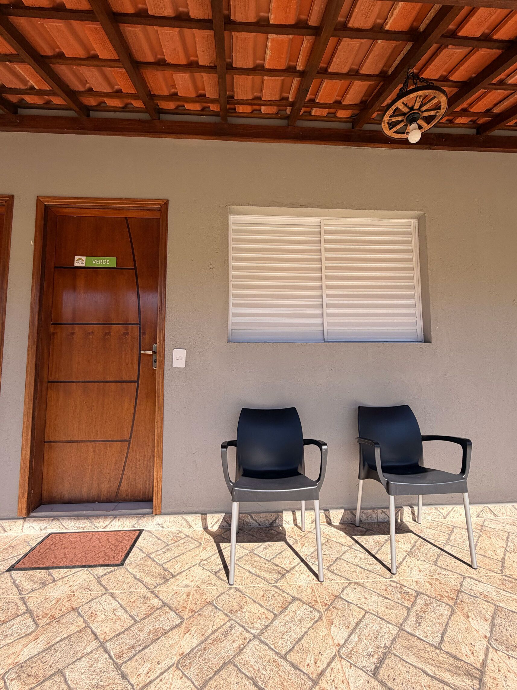 A wooden door with a green sign, two black chairs, a window with blinds, and a tiled floor.
