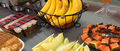 Ein Büfett mit verschiedenen Speisen, darunter Bananen, Melone und ein Glas Orangensaft.