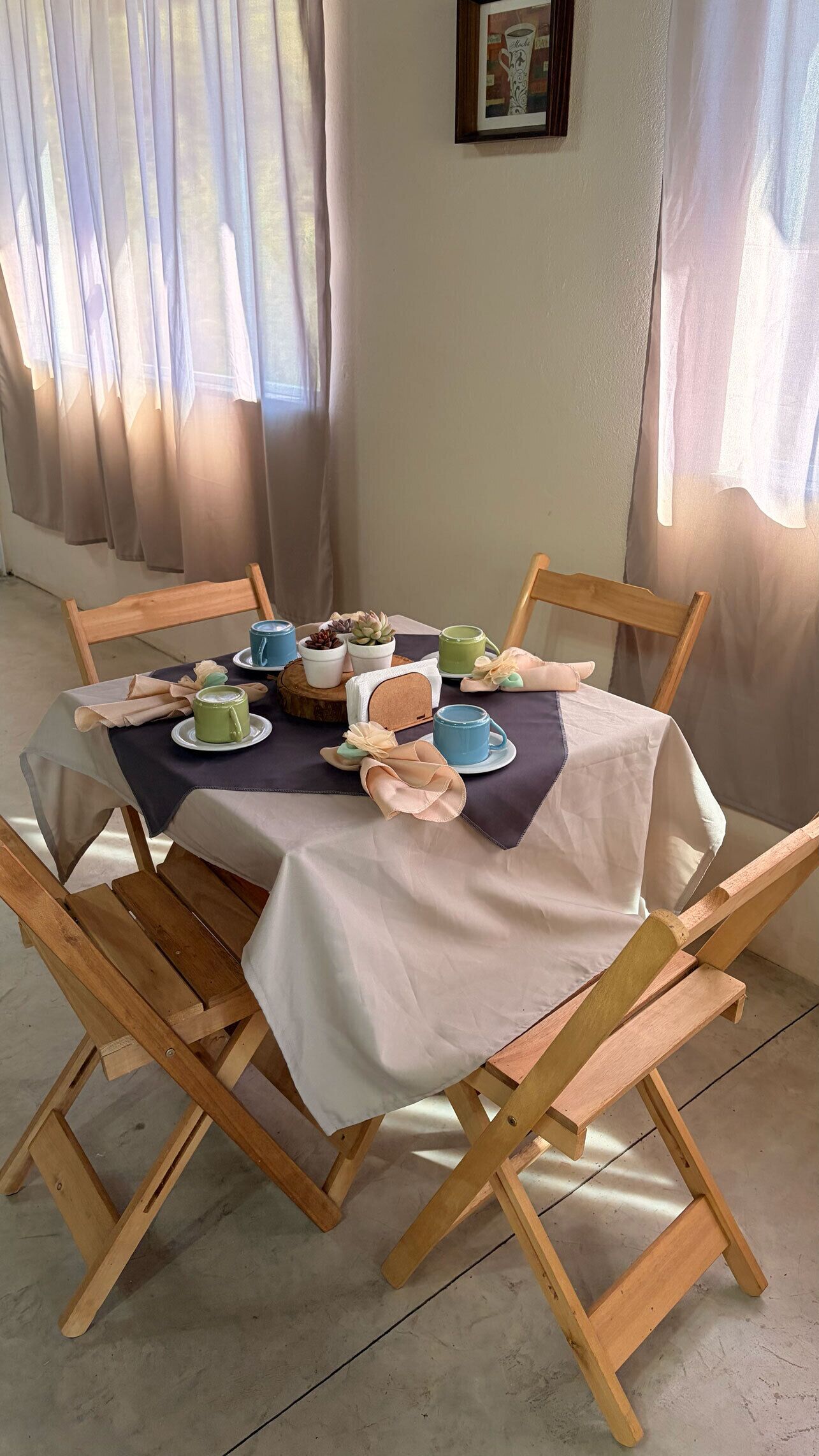 Une table à manger avec des chaises, un tableau encadré au mur et une fenêtre avec des rideaux.