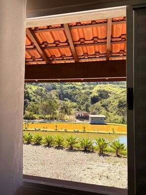 A view from a window with a tiled ceiling and a view of a landscaped area with a pond, plants, and buildings. - Pousada Vale do Arco Íris (Serra Negra)