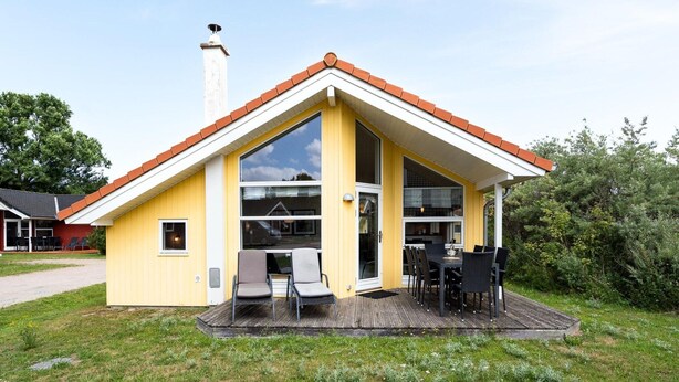 A yellow house with a red roof, a chimney, and a deck with chairs and a table. - Geraumiges Strandhaus in Grobenbrode (Grossenbrode)