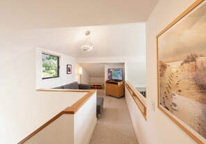 A modern interior with a wooden staircase, a flat-screen TV, and a large painting. - Sea Ridge (TOT ID #2175): 3 BR, 3 BA House in The Sea Ranch, Sleeps 6 (The Sea Ranch)