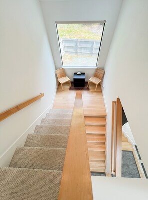 A staircase with a wooden handrail, carpeted steps, and a view of the outdoors through a window. - Sea Ridge (TOT ID #2175): 3  BR, 3  BA House in The Sea Ranch, Sleeps 6 (The Sea Ranch)