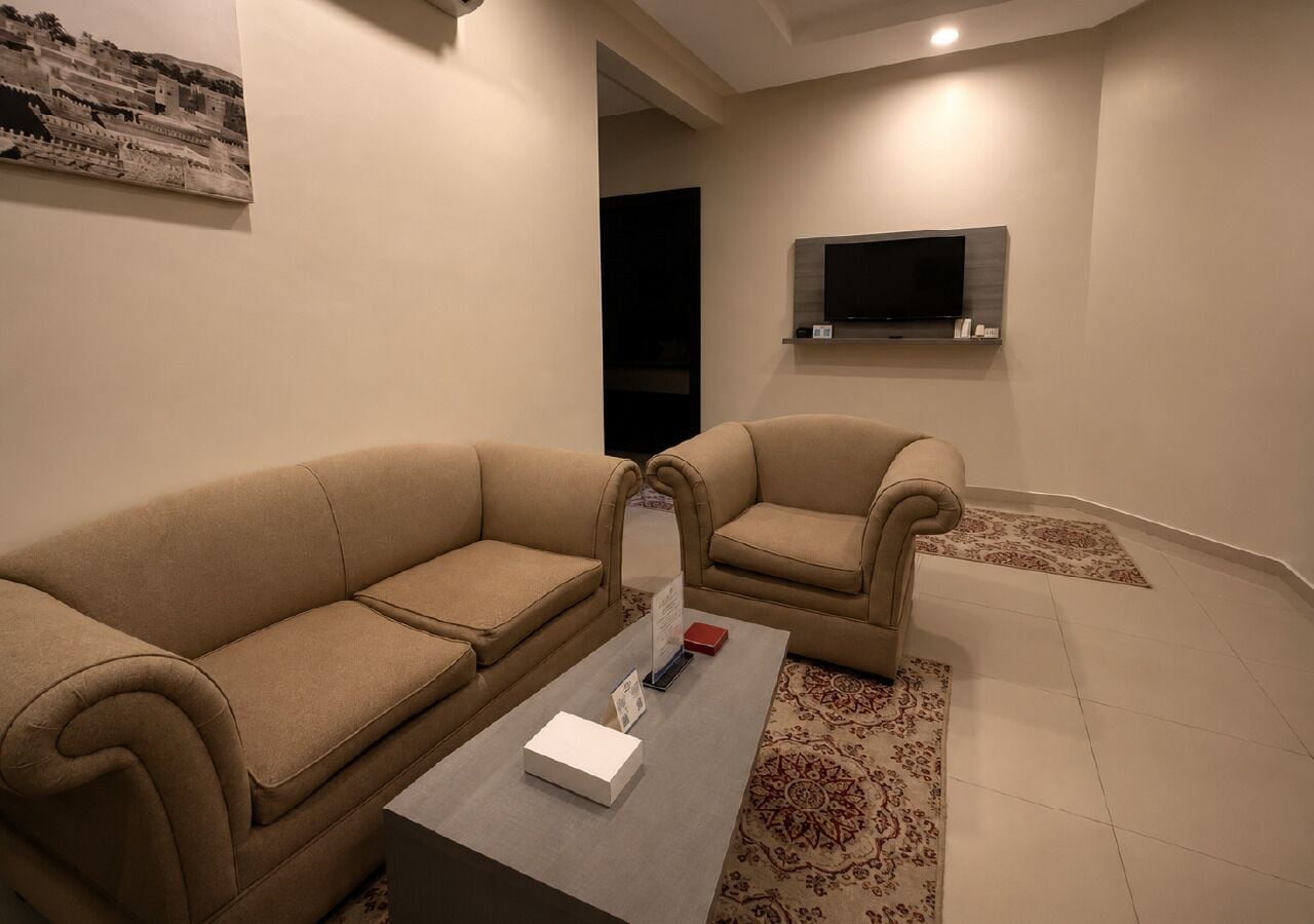 A modern living room with two beige sofas, a coffee table, a flat-screen TV, and a patterned rug.
