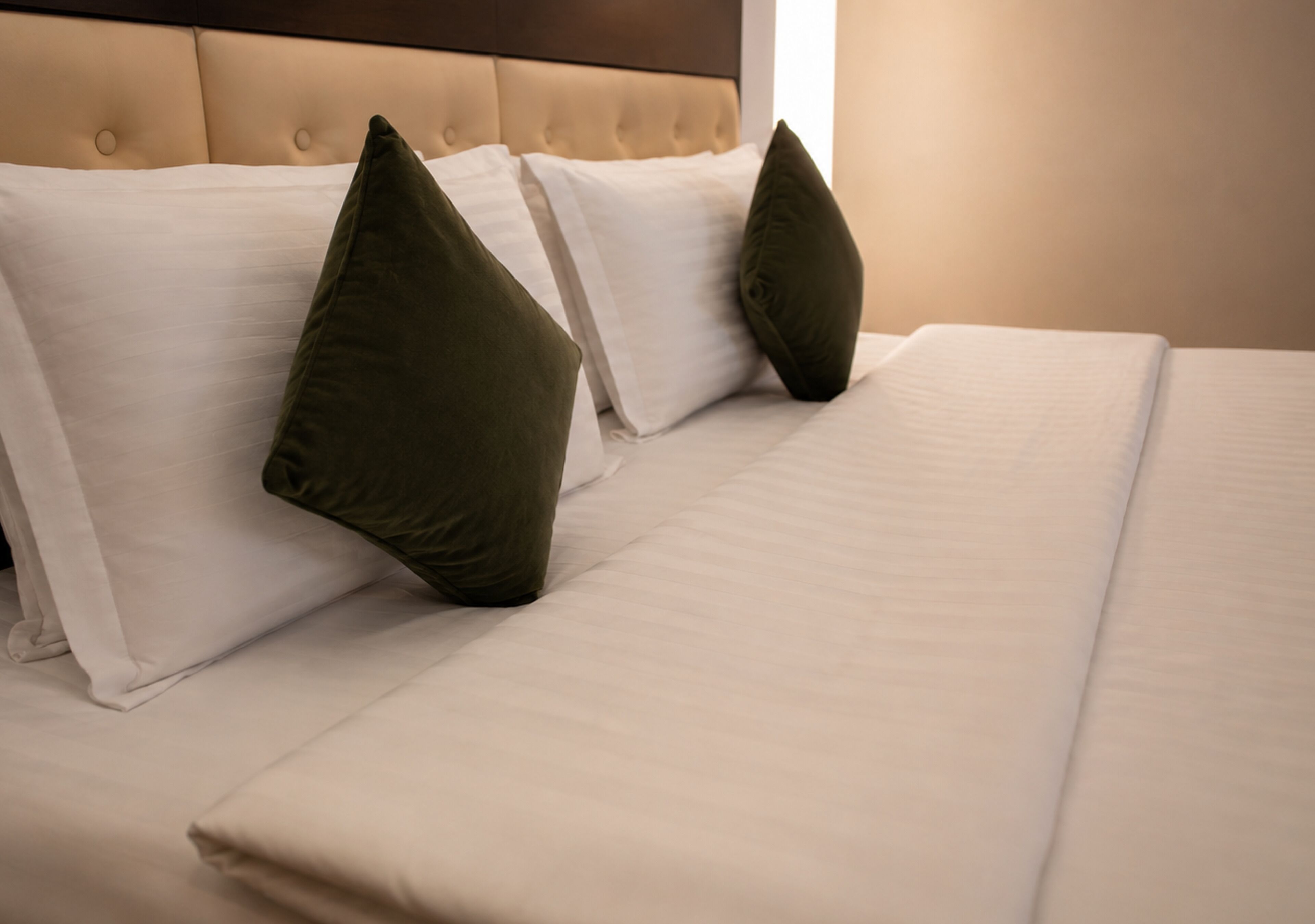 A neatly made bed with white linens and two dark green pillows.
