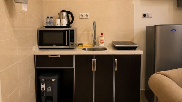 Una kitchenette compacta con microondas, cafetera, lavamanos y refrigerador.