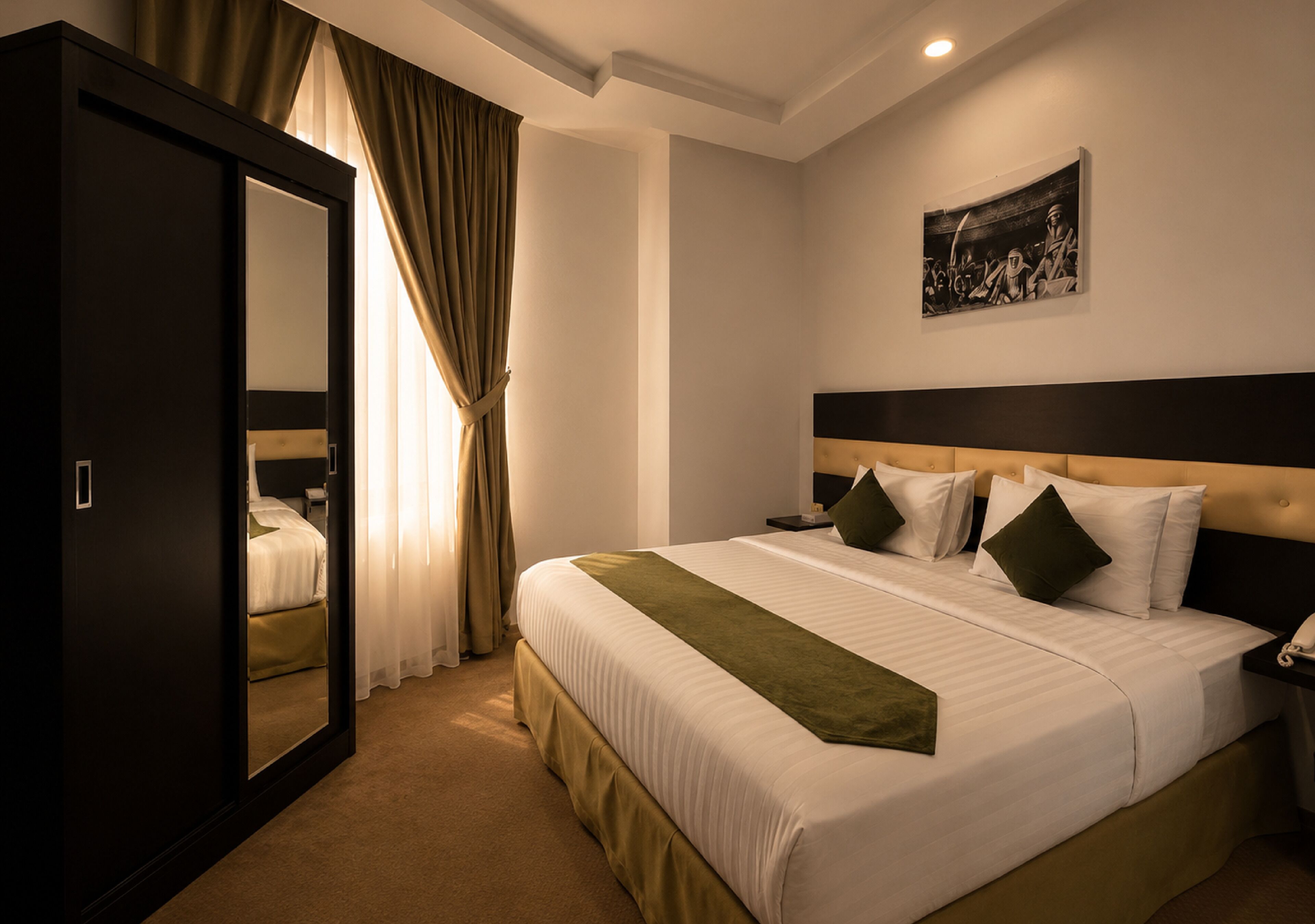 A hotel room with a large bed, a wardrobe, a painting on the wall, and a curtain.