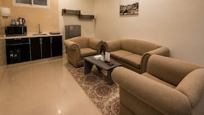 Un salón moderno con un sofá beige, una mesa de centro y una zona de cocina con microondas y refrigerador.