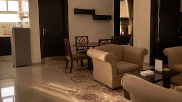 A modern living room with a sofa, chairs, a coffee table, and a rug. There is a kitchen area in the background with a refrigerator and cabinets.