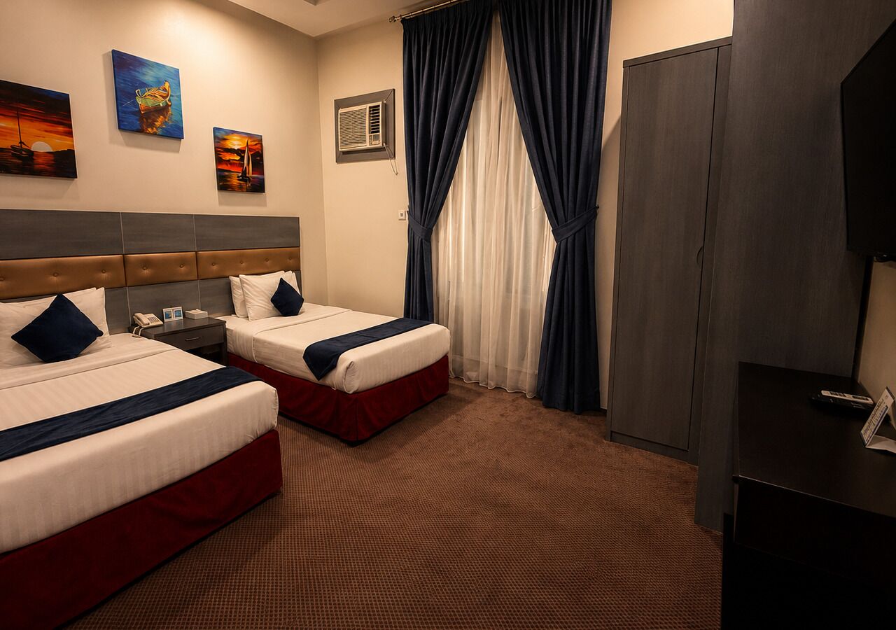 A hotel room with two beds, a wardrobe, a television, and artwork on the wall.