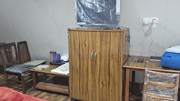 A room with a wooden cabinet, a television on top, a desk with a mobile phone, a chair, and a red patterned rug.