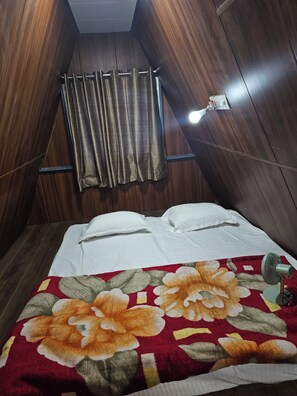 A room with a bed, a floral-patterned blanket, a wall-mounted fan, and a curtain.