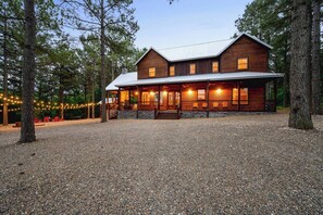 Eine zweistöckige Holzhütte mit Veranda und mehreren Fenstern, umgeben von Bäumen und Kies.