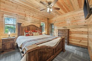 Ein Schlafzimmer mit Holzwandverkleidung, einem Bett, Nachttischen, einer Kommode und einem Deckenventilator.
