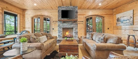 Un interior de cabaña acogedor con chimenea de piedra, mobiliario de madera y un ventanal grande.