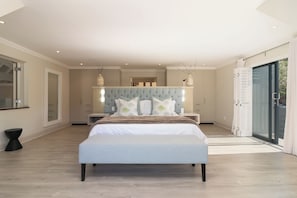 A bedroom with a large bed, a tufted headboard, bedside tables, and a sliding glass door to the outside.