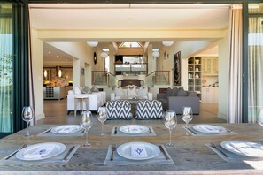 A spacious living area with a dining table set for four, a staircase leading to an upper level, and a kitchen visible in the background. - Stunning 5-bedroom spacious house with pool in Knysna. A perfect for family home (Knysna)