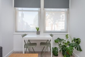 A room with a white desk, two chairs, a small potted plant, and large green plants near the windows. - Fulham Duplex Near Parsons Green Station (London)