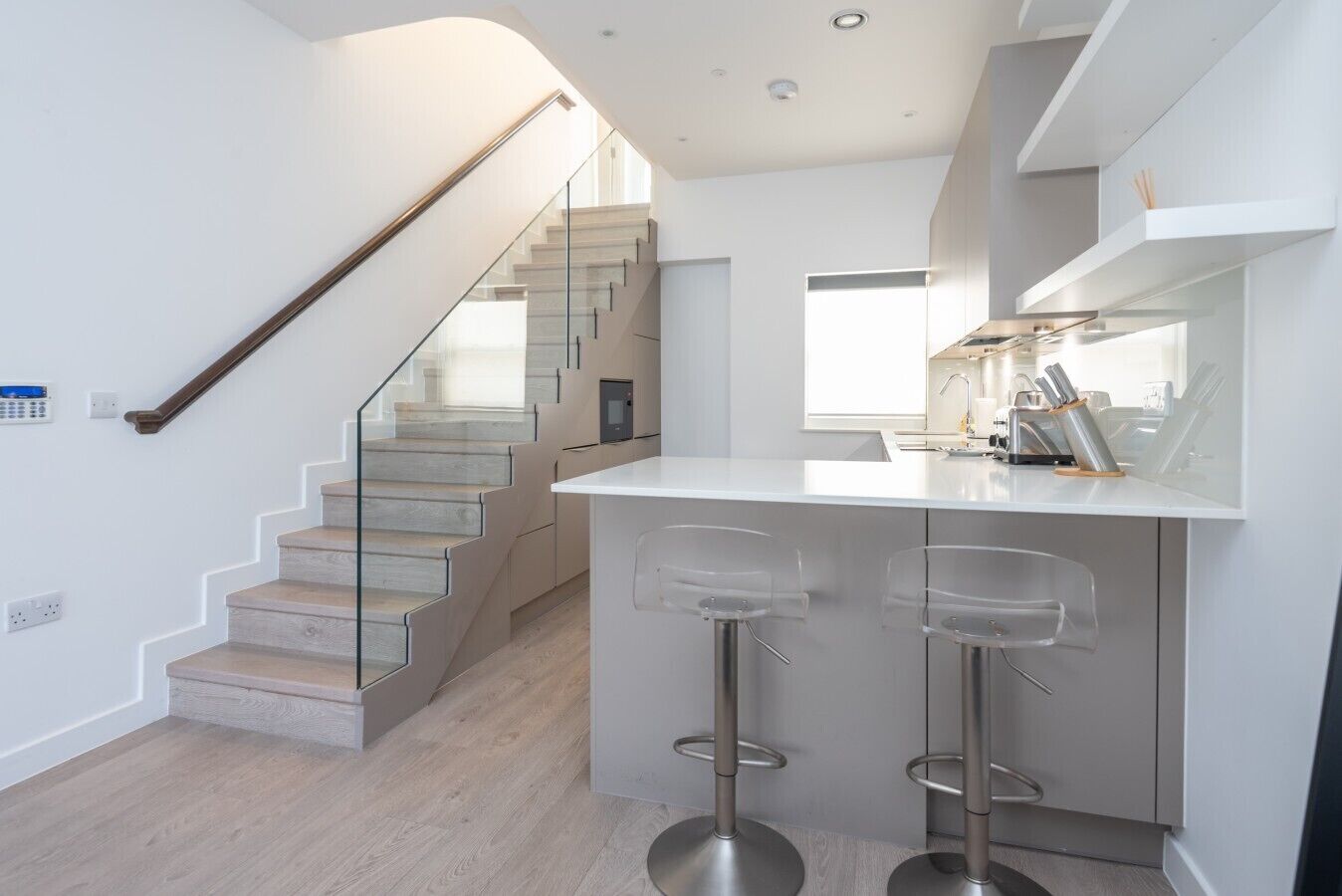 Een moderne keuken met een centraal eiland, barkrukken en een trap naar een hoger gelegen verdieping.
